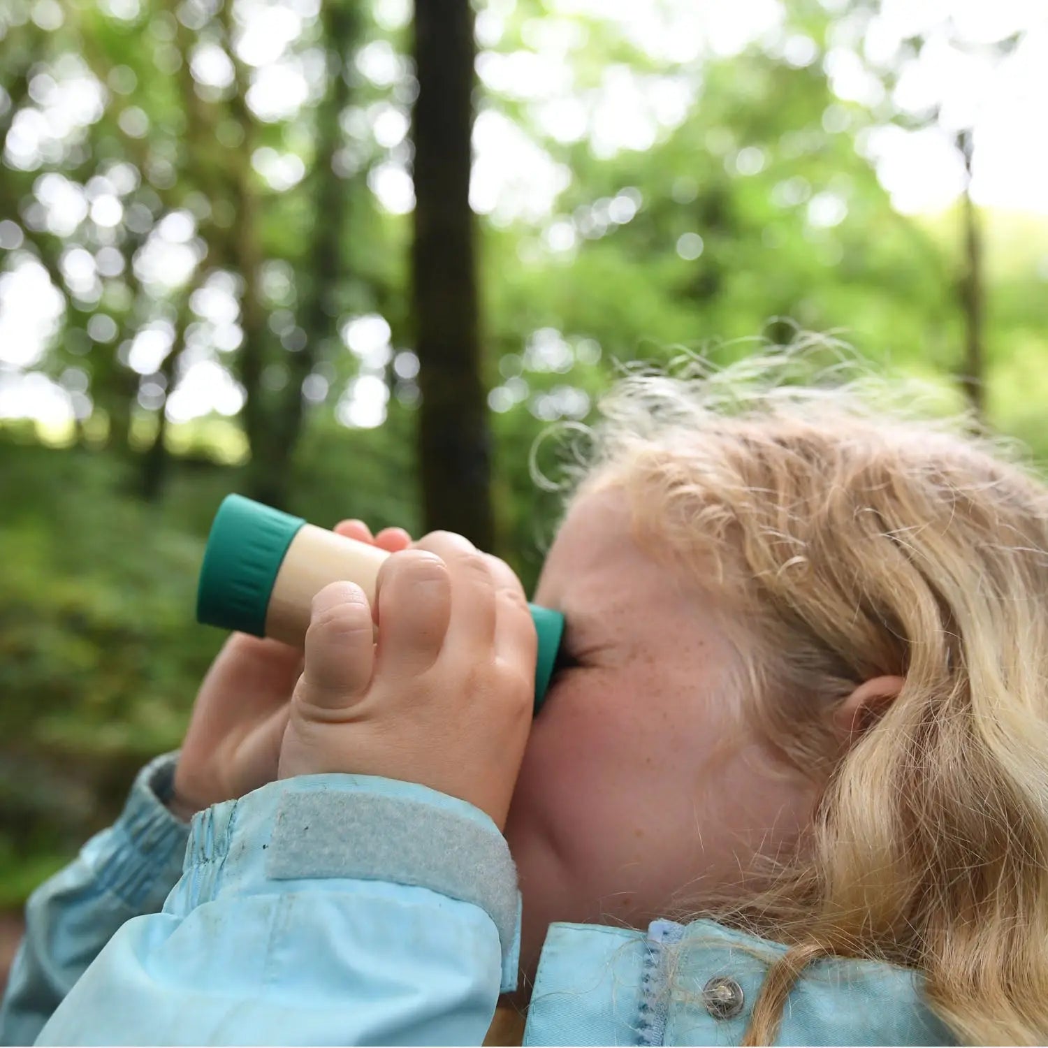 Blonde girl looking through a small monocular in a lush, green forest