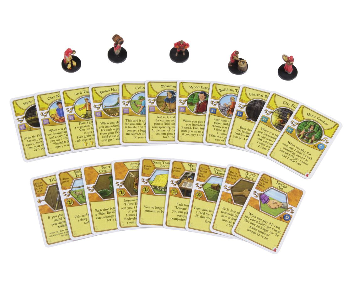 Board game components: small worker miniatures and fanned-out resource cards, some with farming illustrations.