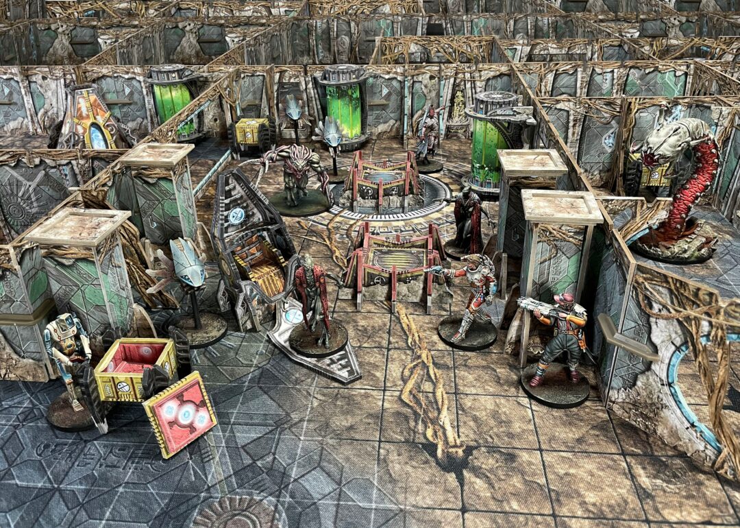 Sci-fi tabletop wargame with diverse miniatures battling amidst detailed futuristic terrain, walls, and glowing green tanks.