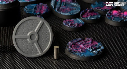 Gray, textured underside of a miniature base next to a stack of magnets. Several colorful, painted sci-fi bases are in the background.