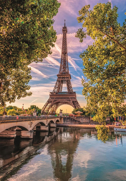 The Eiffel Tower rises above a bridge on the Seine River, framed by trees, its reflection visible in the water at dusk.