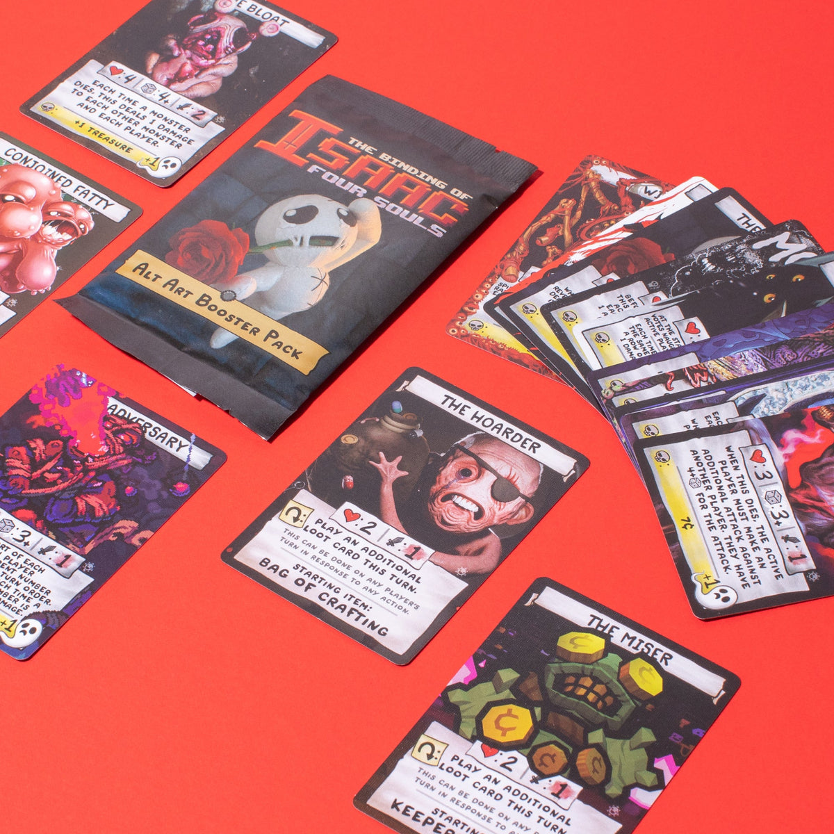 The Binding of Isaac Four Souls game booster pack and monster cards scattered on a vibrant red background