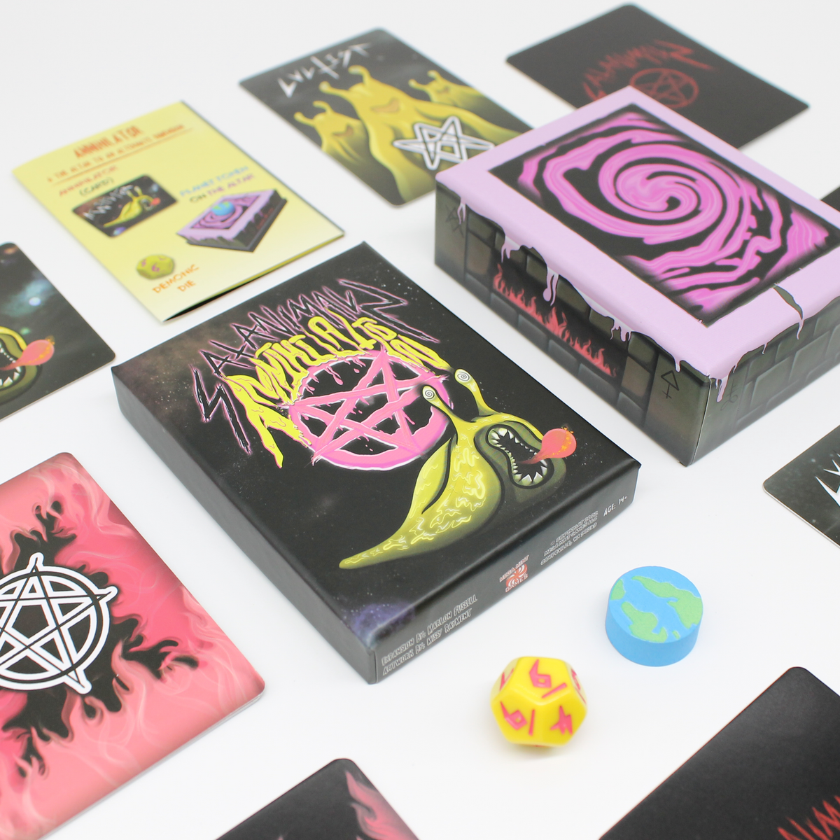 Annihilator card game components displayed, black box with a yellow slug monster, pink-topped box, cards, yellow die, and Earth token