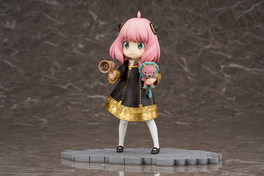 Anya Forger figure in a black dress, holding a megaphone and a pink Chimera plush on dark background