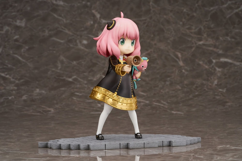 Anya Forger figure in a black dress, holding a megaphone and a pink Chimera plush on dark background