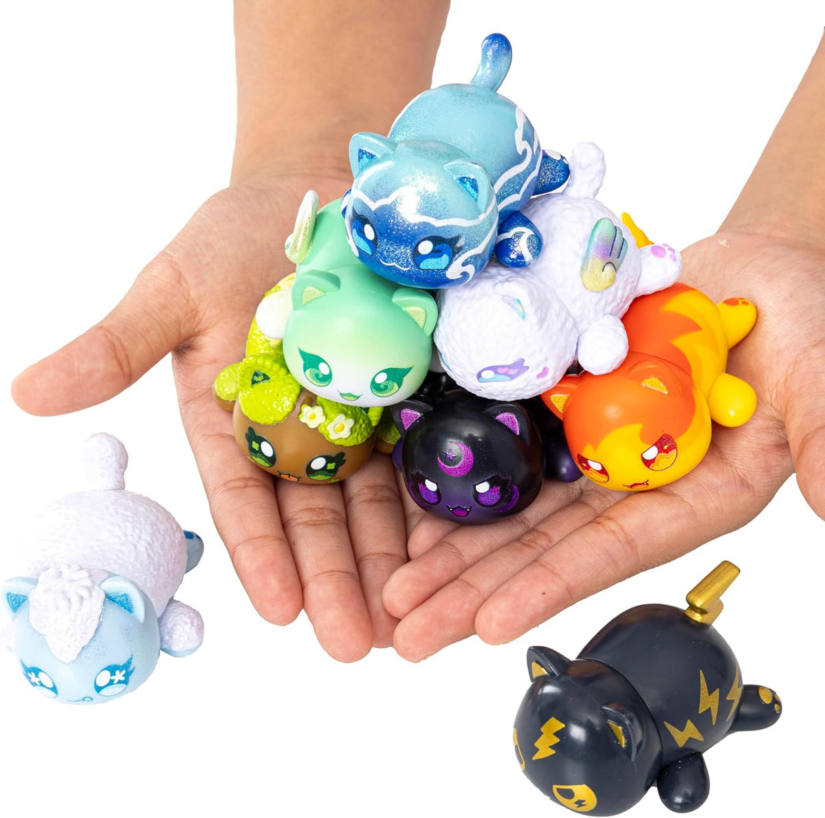 A person&#39;s hands hold a pile of diverse, colorful cat toy figures, with two more nearby on a white surface