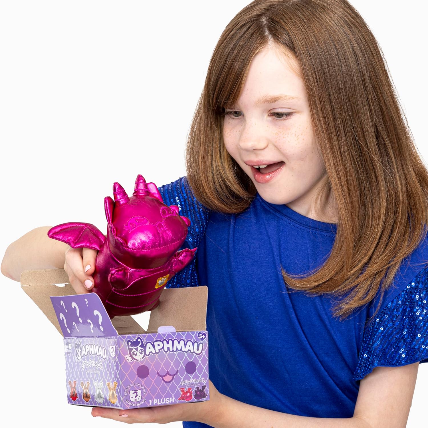 Young girl excitedly pulls a shiny pink dragon plush from an "APHMAU" blind box