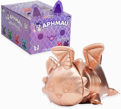 Shiny rose gold dragon plush toy lies beside a purple Aphmau MeeMeows Mystery Plush box