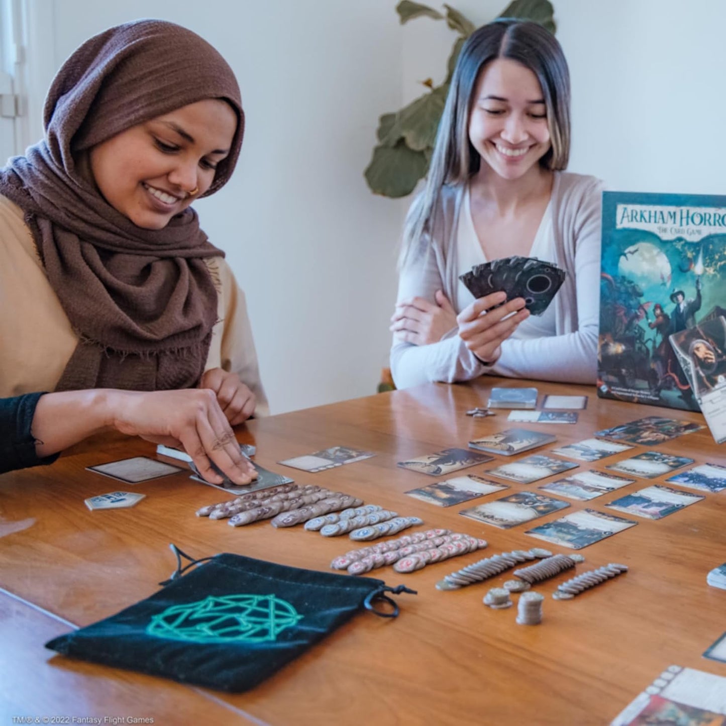 Two smiling women playing Arkham Horror: The Card Game. One selects a card, the other holds cards