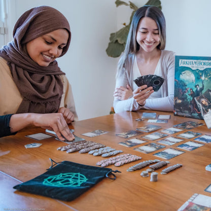 Two smiling women playing Arkham Horror: The Card Game. One selects a card, the other holds cards