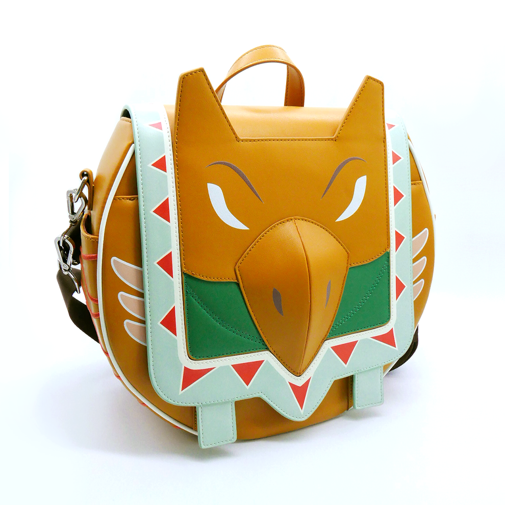 Brown bird-faced bag with a sharp beak, white stylized eyes, green chest, and light blue trim adorned with red triangles.