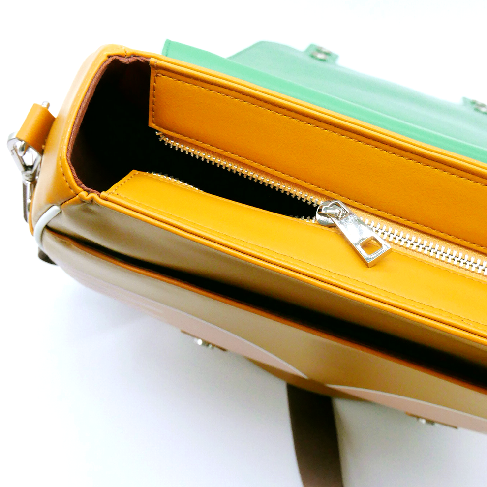 Mustard yellow bag with a partially unzipped silver zipper. A mint green flap is visible behind.