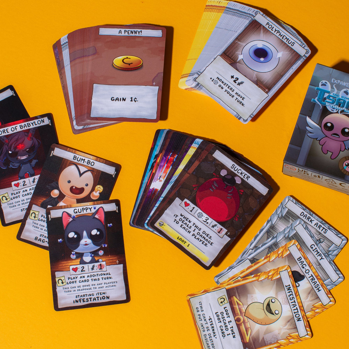 A collection of colorful game cards from The Binding of Isaac: Four Souls, laid out on a bright yellow surface