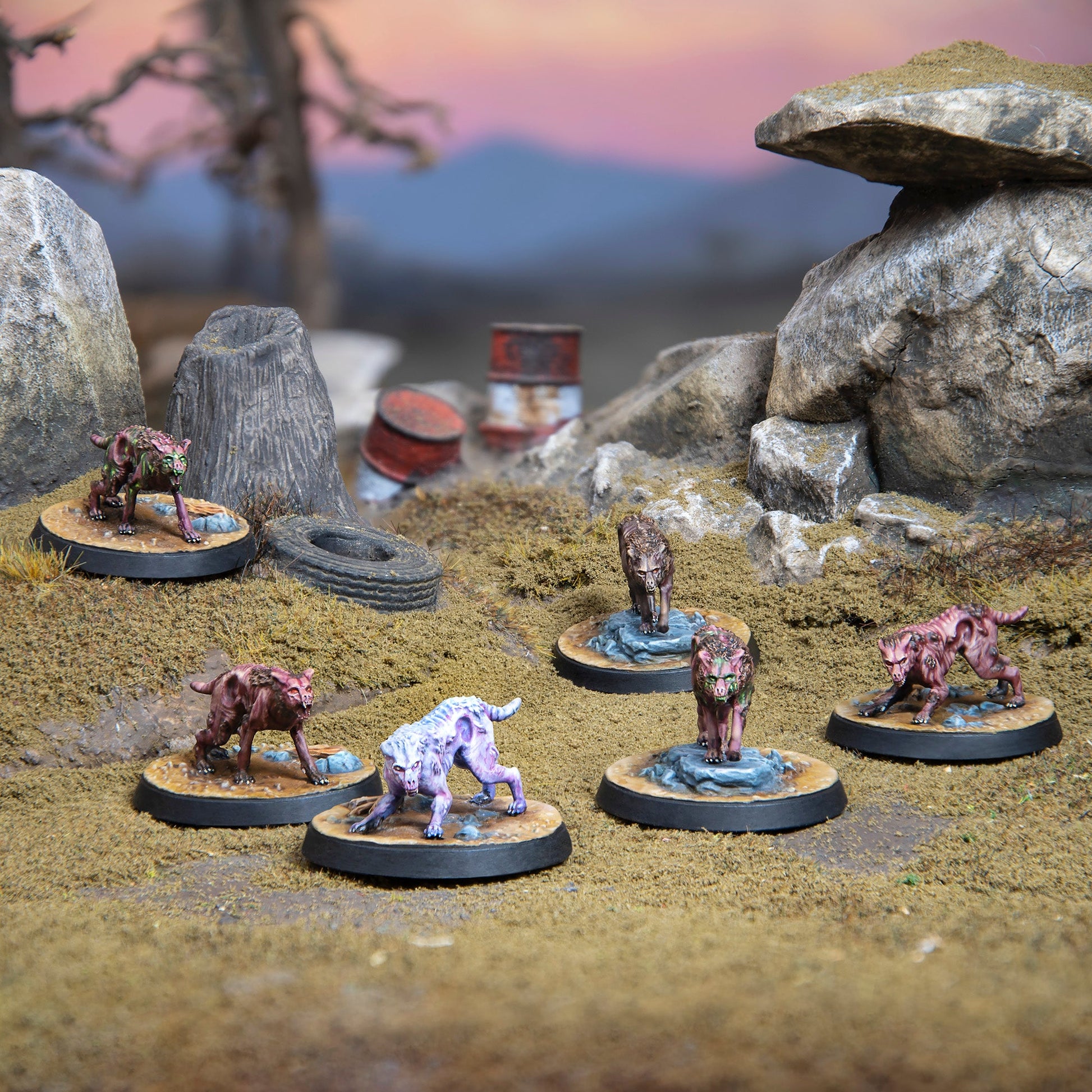 Six mutated, dog-like miniatures, some with green glowing parts, crouch menacingly on a rocky wasteland with barrels