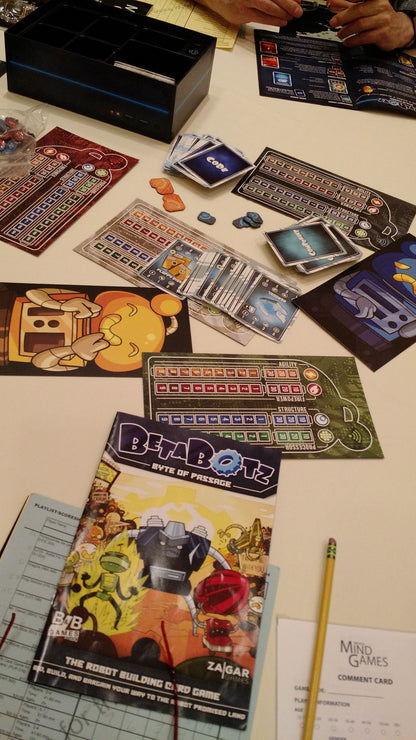 Overhead view of a table with the BetaBotz: Byte of Passage card game, showing cards, tokens, game boards, and a player's hands.
