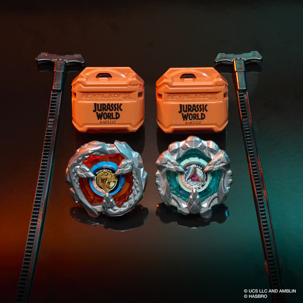 Two Beyblade X Jurassic World spinning tops (T-Rex & Pteranodon), cases and launchers displayed on a dark surface
