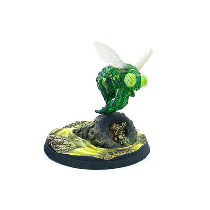 Green fly monster miniature with large bright green eyes and clear wings, standing on a dark base with yellow-green ooze and debris