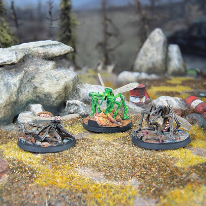 Three mutant insect miniatures on a rocky diorama - a bright green insect feeds on a corpse, while two grey insects stand nearby