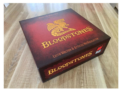 Red Bloodstones board game box with a gold dragon logo and title on a light wooden table, angled view.