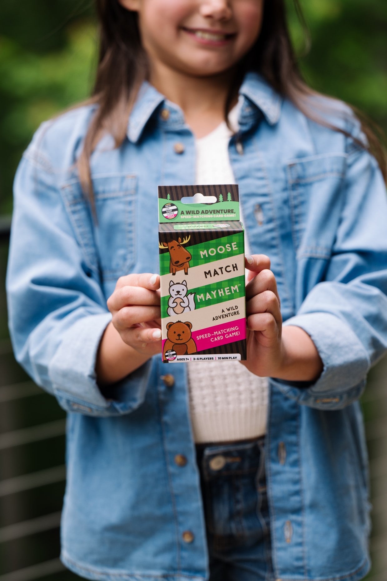 Smiling child holds the "Moose Match Mayhem" speed-matching card game box outdoors