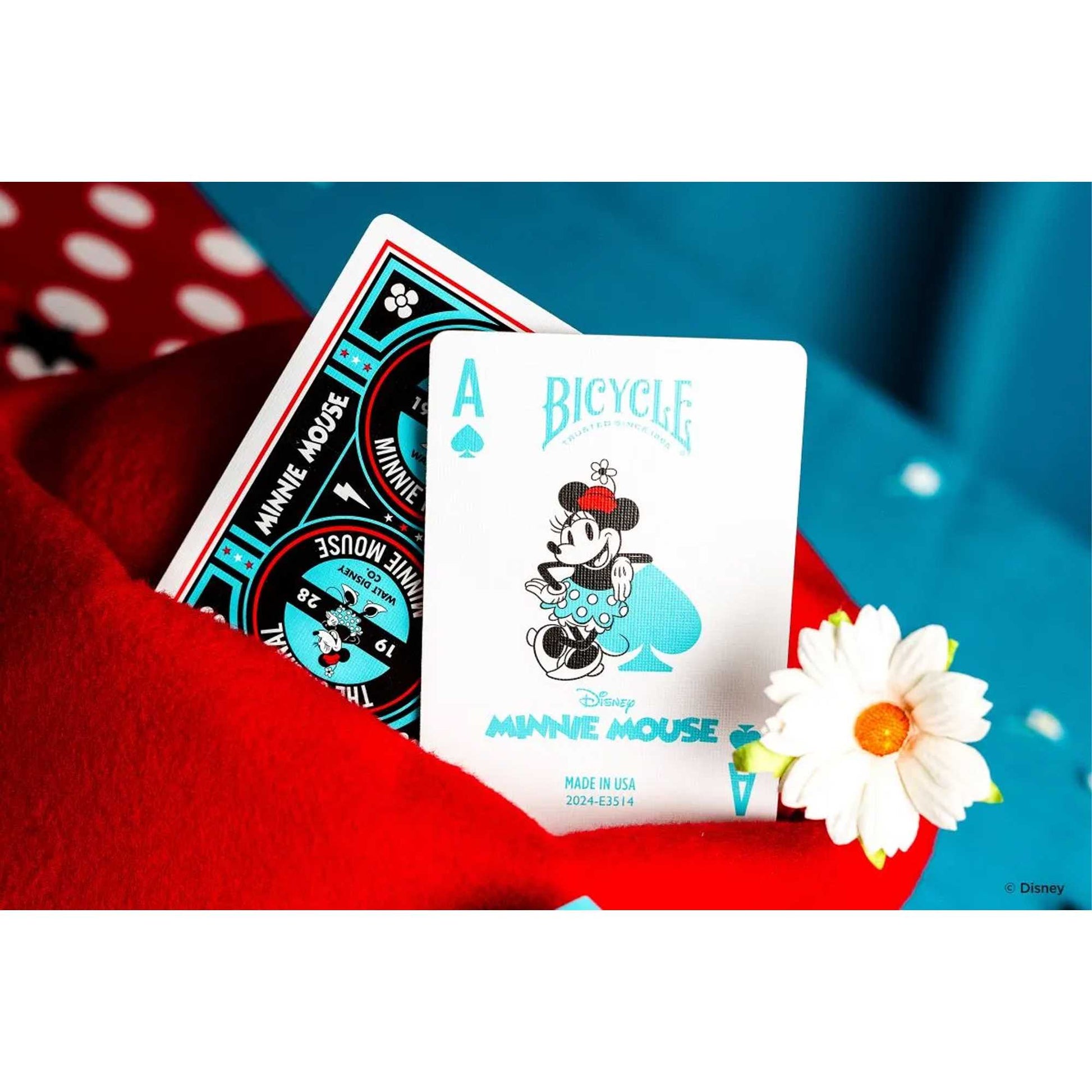 Minnie Mouse Bicycle Ace of Spades playing card, featuring a teal illustration, resting on red fabric next to a daisy