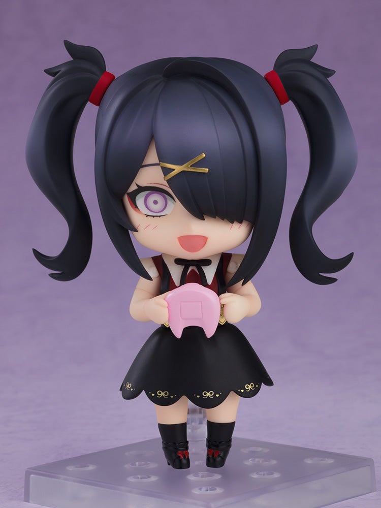 Smiling Nendoroid figure with black pigtails, gold X barrette, purple eyes, black dress, holding a pink controller