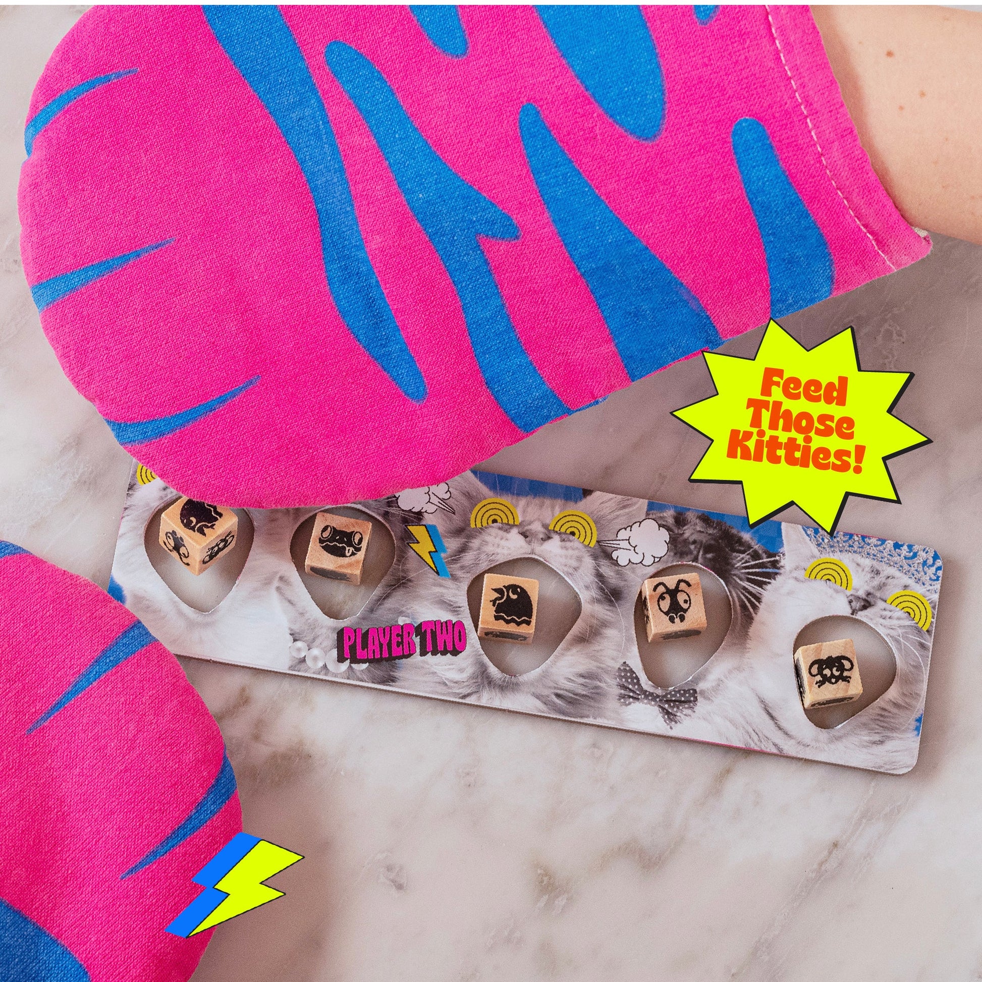 A vibrant "Feed Those Kitties" board game shows cat faces wooden pieces and pink & blue patterned fabric "Player Two" is visible