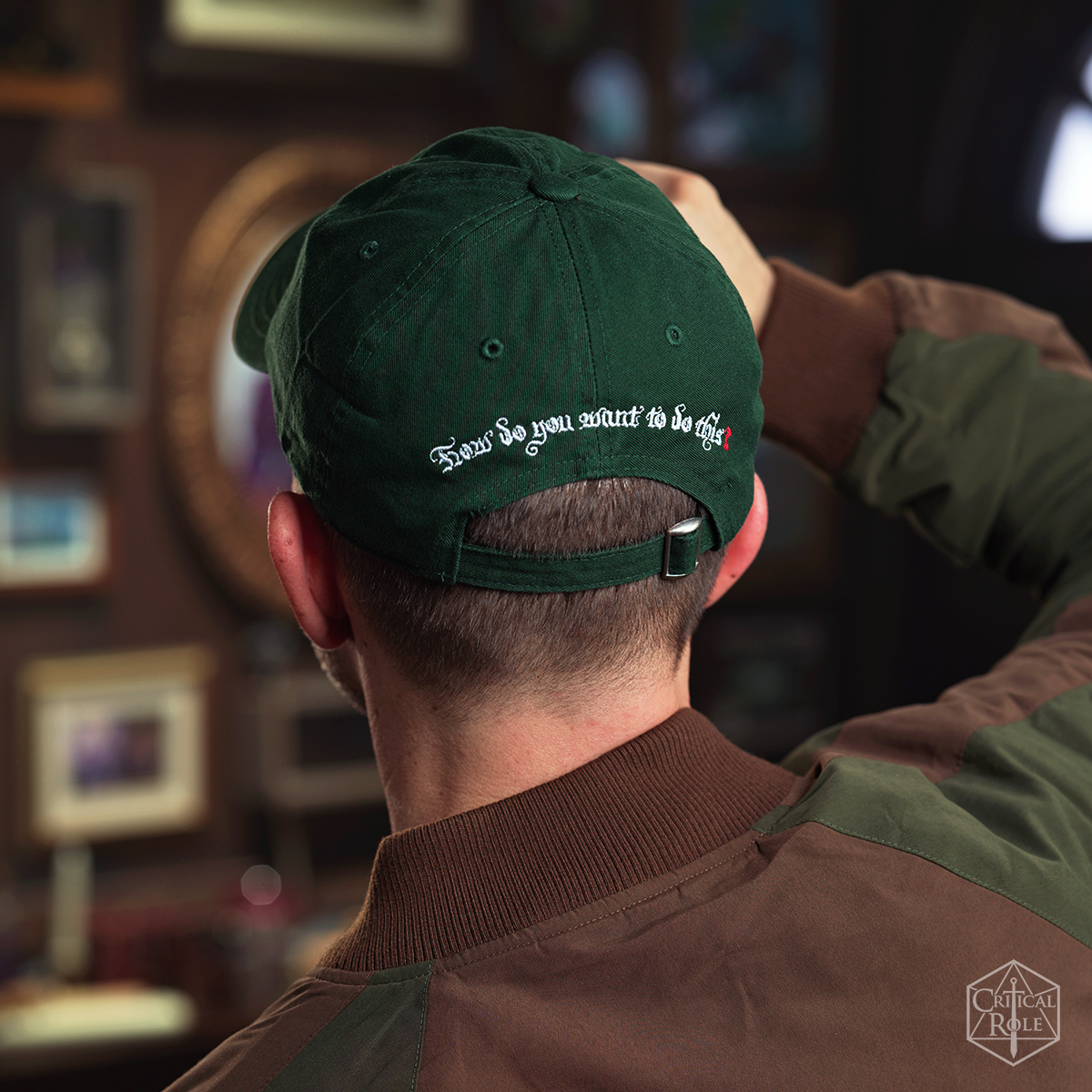 Back of a person wearing a dark green Critical Role Dad hat embroidered with "How do you want to do this," hand touching it