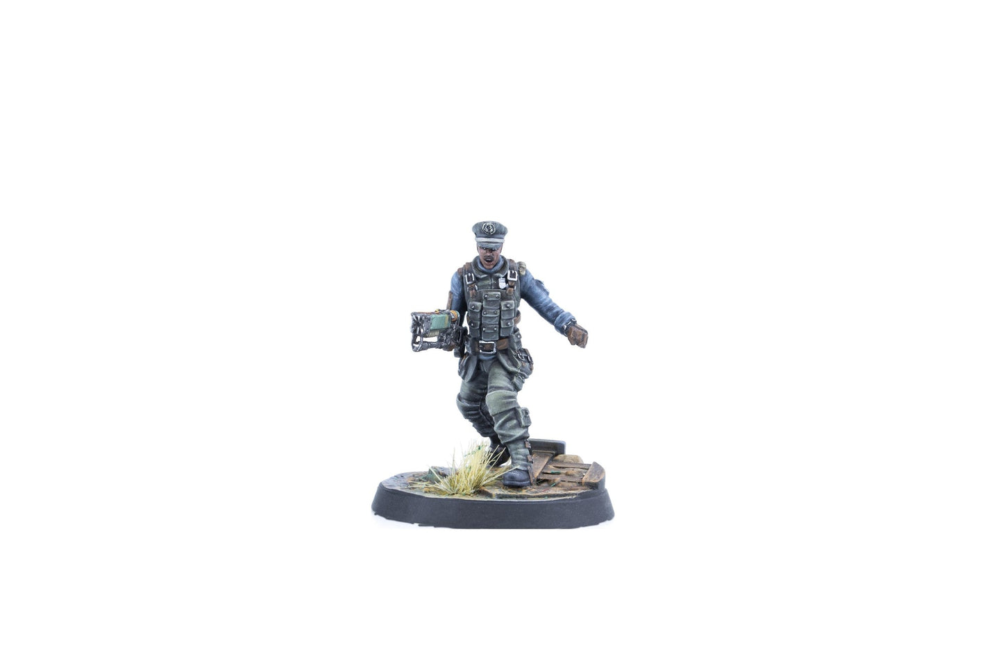 A miniature figure of a man in a grey-blue uniform, tactical vest, and peaked cap, holding a unique green weapon, striding on a base
