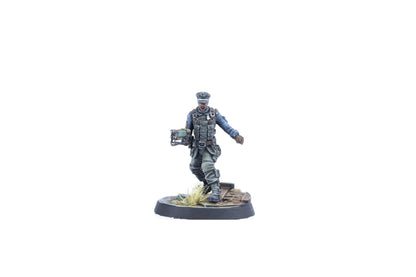 A miniature figure of a man in a grey-blue uniform, tactical vest, and peaked cap, holding a unique green weapon, striding on a base