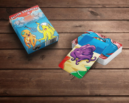 A "Fallen Treasures" card game box featuring two cartoon octopuses, next to a stack of cards with a purple octopus, on wood.
