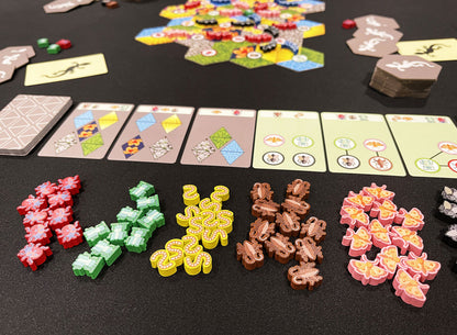 A colorful board game setup: hexagonal map tiles, cards, and piles of wooden tokens like spiders, worms, and butterflies