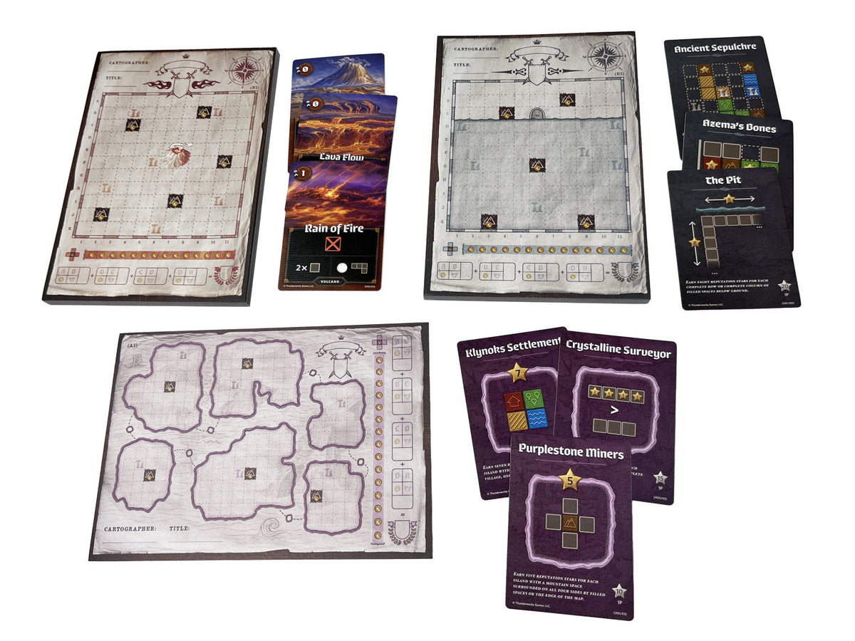The Cartographers Map Pack Collection laid out, featuring three unique gridded map sheets and multiple stacks of thematic game cards for diverse gameplay