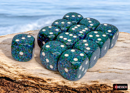 Twelve speckled green-blue dice with white pips, mostly sixes, are stacked on driftwood by a blue ocean