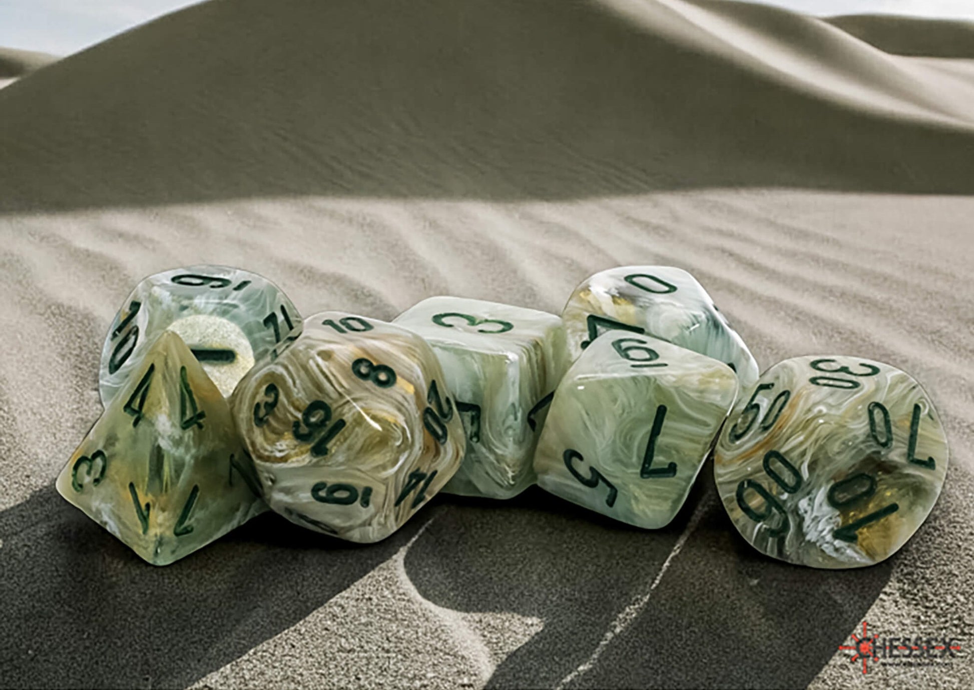 Translucent green/gold swirled polyhedral dice with dark numbers lie on rippled sand with desert dunes behind