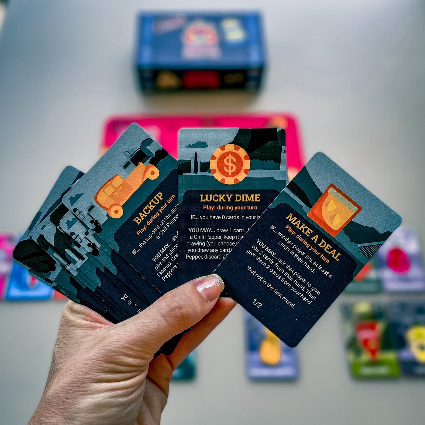 Person holding Chili Mafia Goodfellas Expansion card game cards showcasing Backup Lucky Dime and Make a Deal action cards with unique illustrations