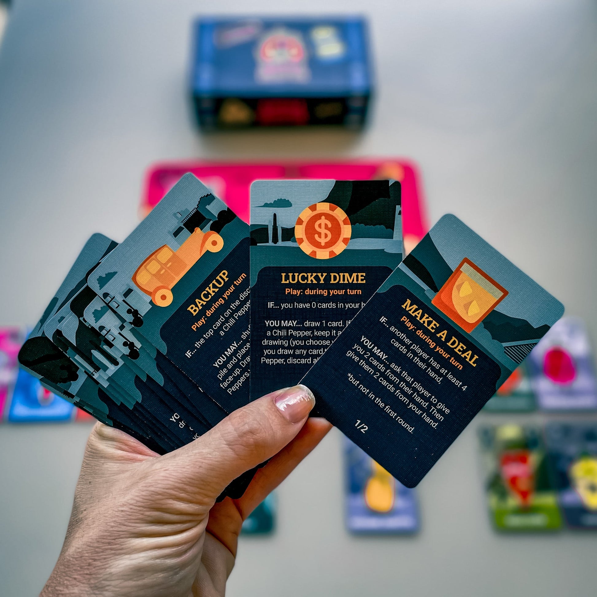 Person holding Chili Mafia Goodfellas Expansion card game cards showcasing Backup Lucky Dime and Make a Deal action cards with unique illustrations