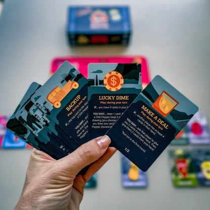 Person holding Chili Mafia Goodfellas Expansion card game cards showcasing Backup Lucky Dime and Make a Deal action cards with unique illustrations