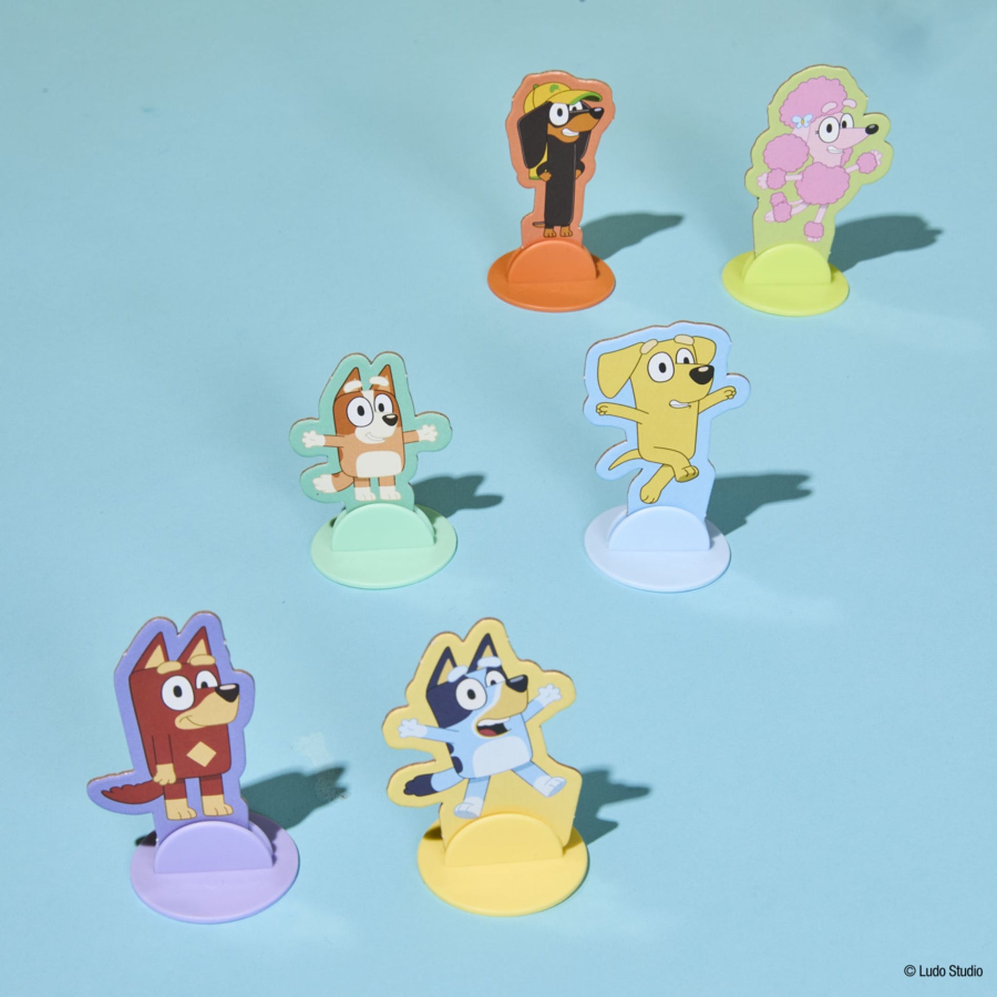Six colourful Bluey character standees (Chloe, Lucky, Jean-Luc, Indy, Rusty, Winton) on various coloured bases, against a light blue background