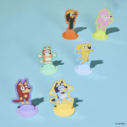 Six colourful Bluey character standees (Chloe, Lucky, Jean-Luc, Indy, Rusty, Winton) on various coloured bases, against a light blue background
