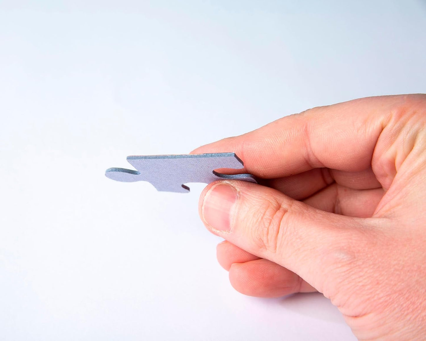 A hand holds a single gray puzzle piece against a white background