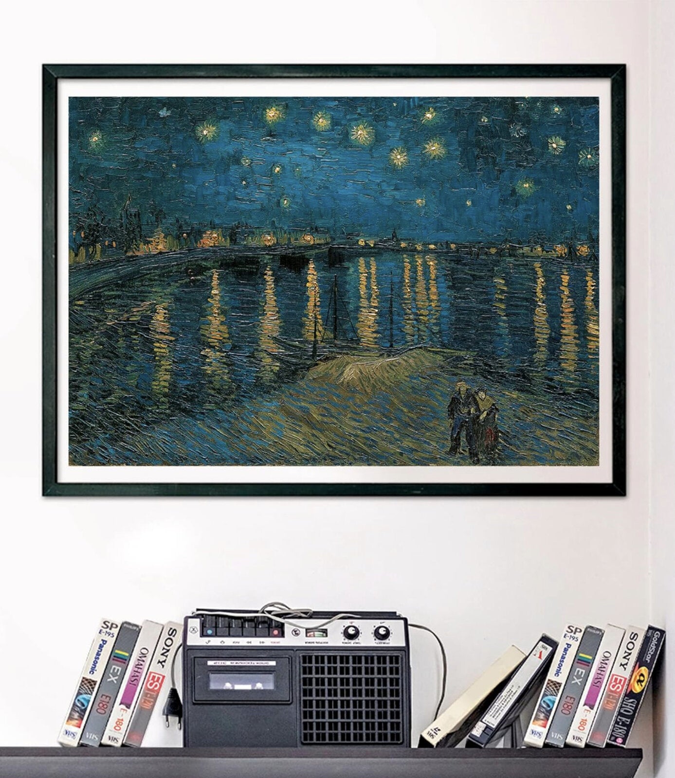 A framed print of Van Gogh's Starry Night Over the Rhone hangs above a shelf with a cassette player and stacked VHS tapes