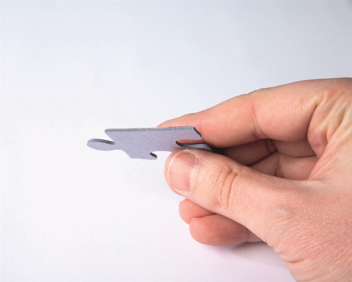 Close-up of a hand holding a single gray puzzle piece against a white background