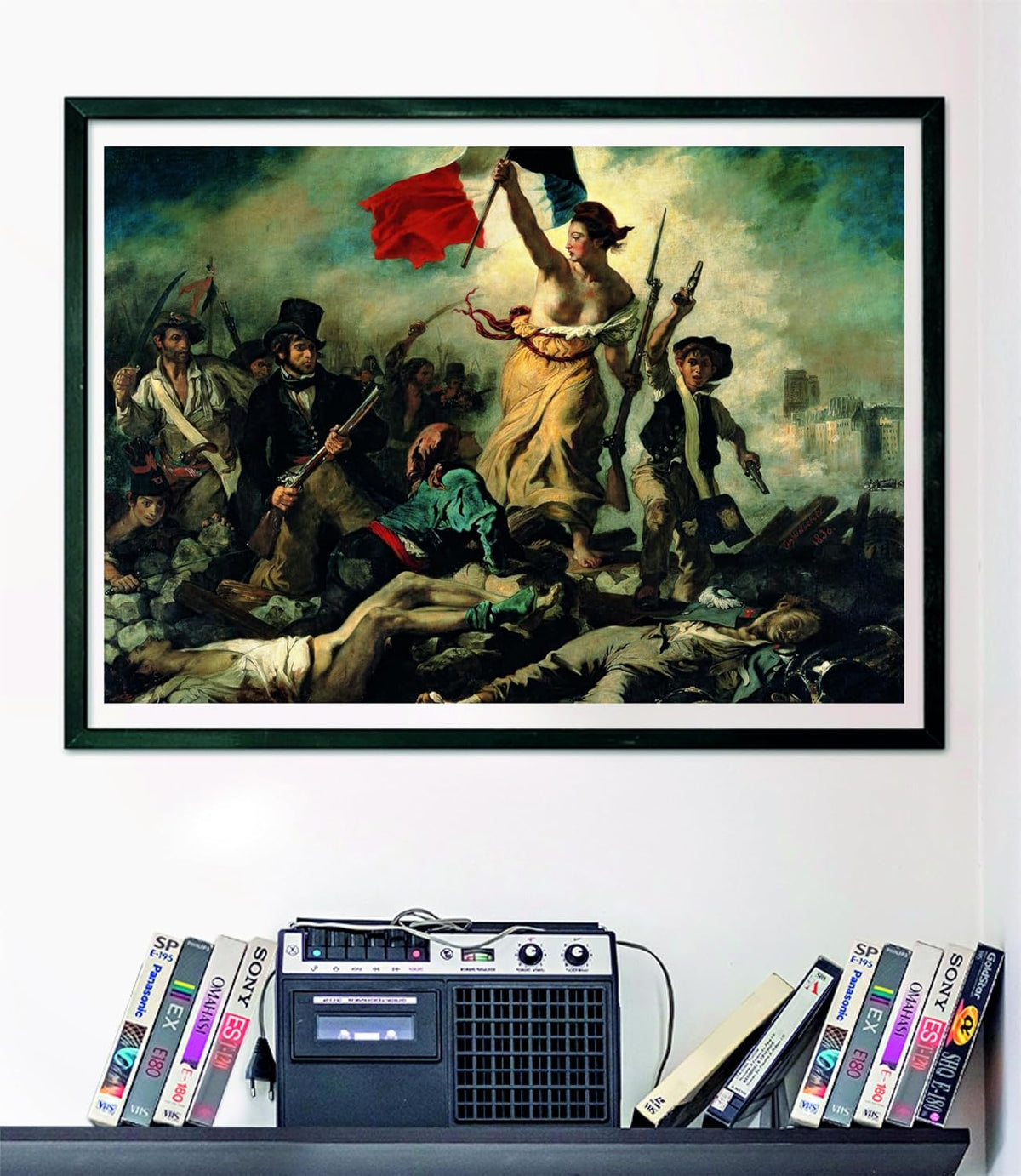 A framed puzzle of Liberty leading armed revolutionaries with a French flag hangs above a cassette player &amp; VHS tapes