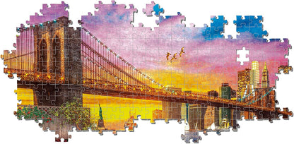 An unfinished jigsaw puzzle depicting the Brooklyn Bridge and NYC skyline at dusk, with a vibrant pink and orange sky