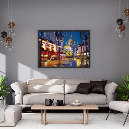 Framed painting depicts Sacré-Cœur, an illuminated cafe, and a wet Paris street with reflections at night