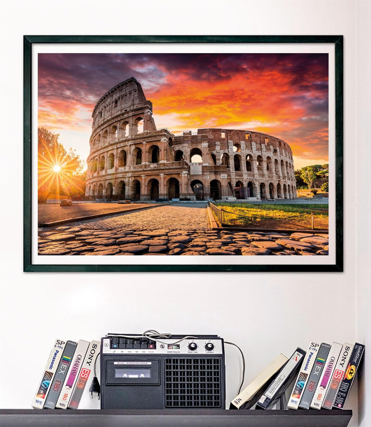 The Colosseum at sunset with a dramatic orange sky, sunburst, and cobblestone path