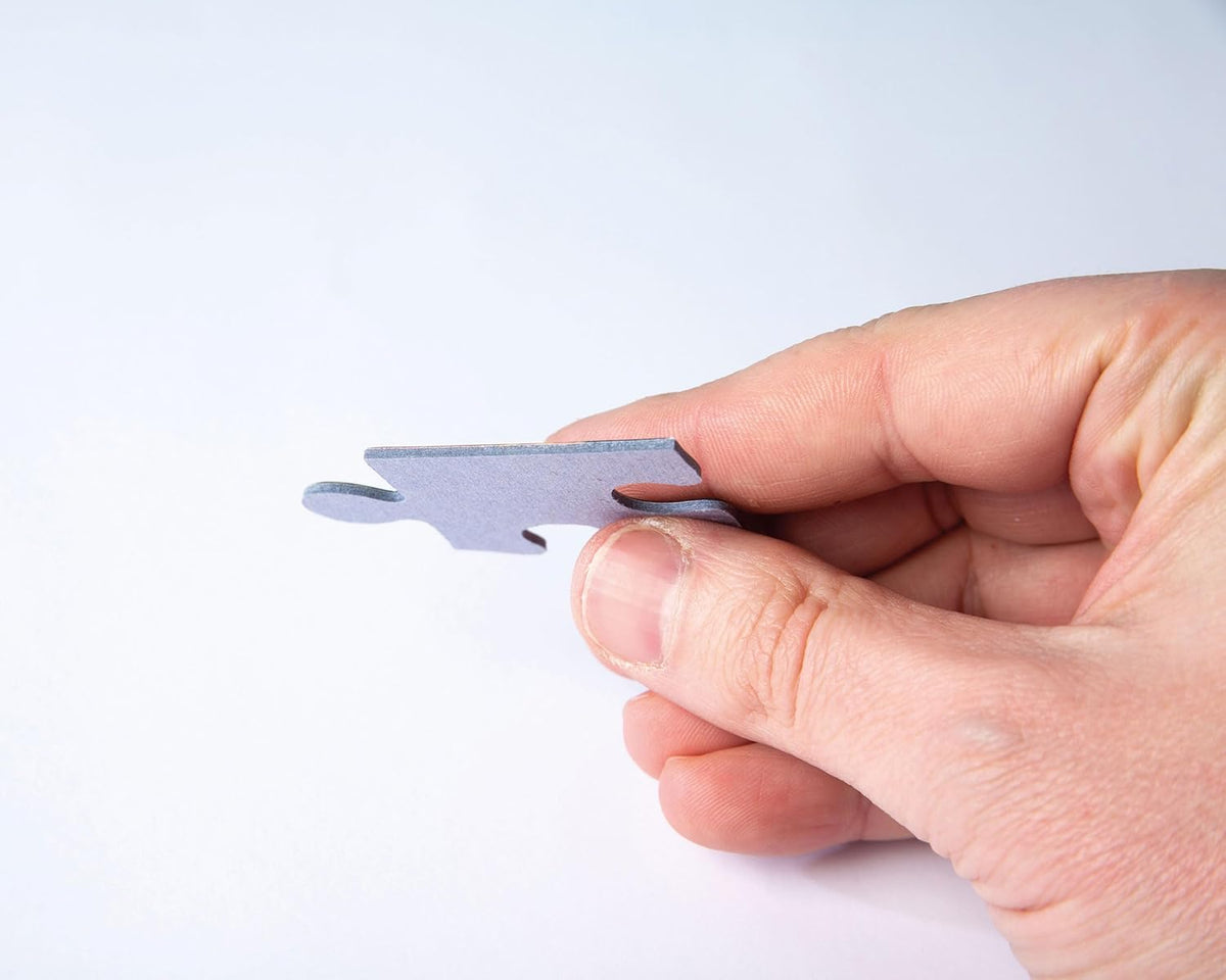 A hand holds a light gray puzzle piece between its thumb and forefinger against a white background