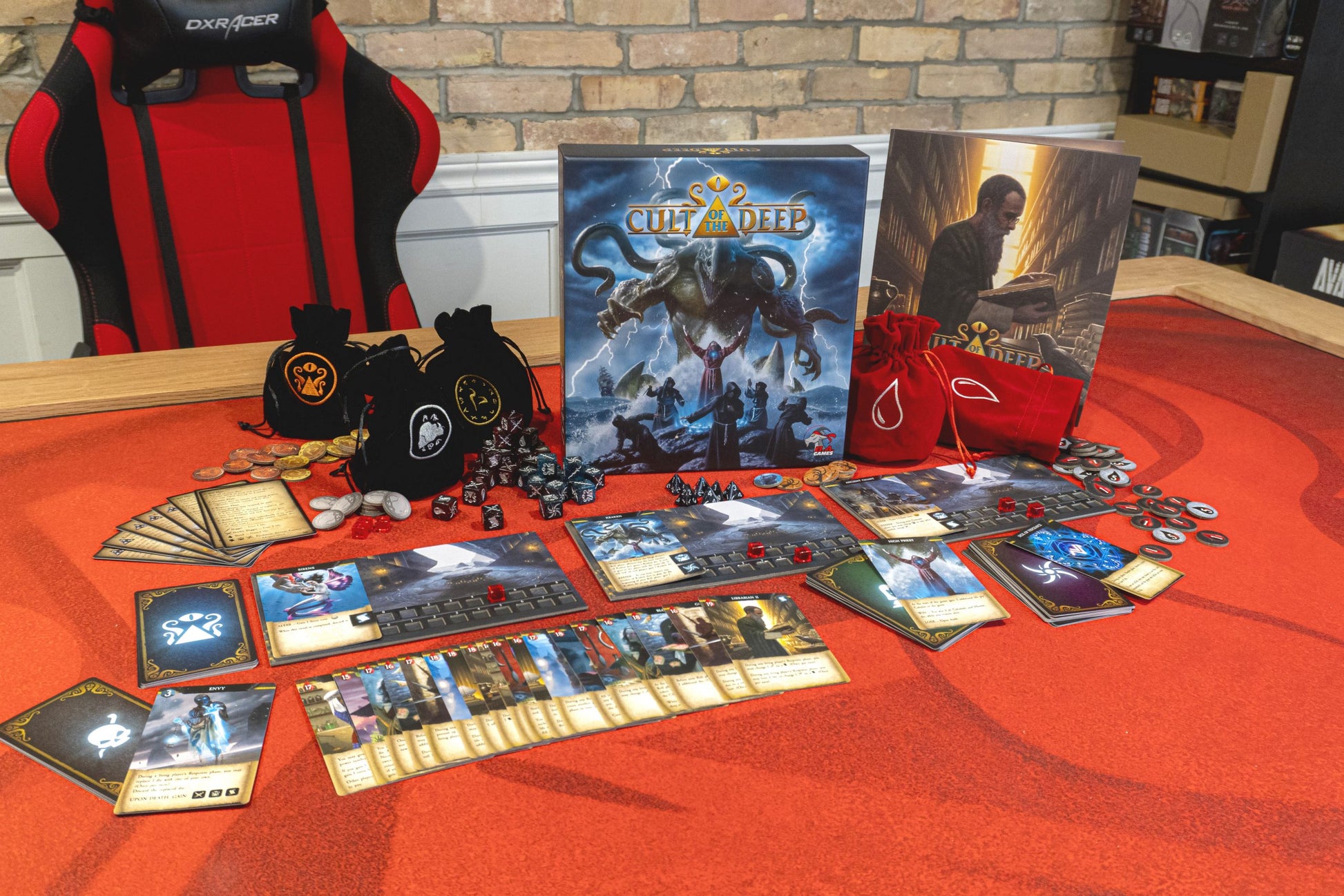 Cult of the Deep board game box and components laid out on a red mat: cards, dice, tokens, and bags