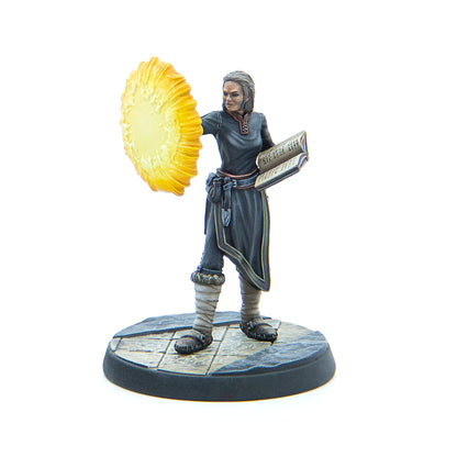 Painted miniature of a female spellcaster in grey robes, reading a book and projecting a bright yellow magical shield